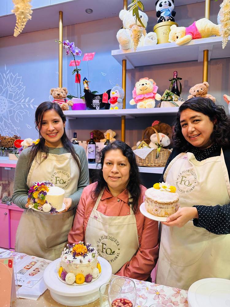 Tres mujeres sonríen con mandil mostrando las tortas con flores que decoraron